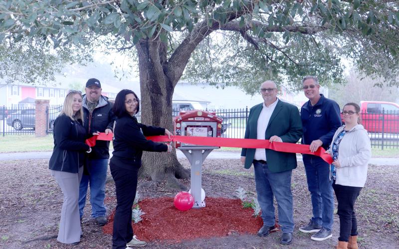 Dr. Kathia Ortiz cuts the ribbon joined by Nassau County commissioners Klynt Farmer and “Hupp” Huppmann, Callahan Town Clerk Shawna Gugliuzza, Callahan Mayor Randy Knagge, and Tiny Libraries of Nassau President Katey Kilpatrick. 