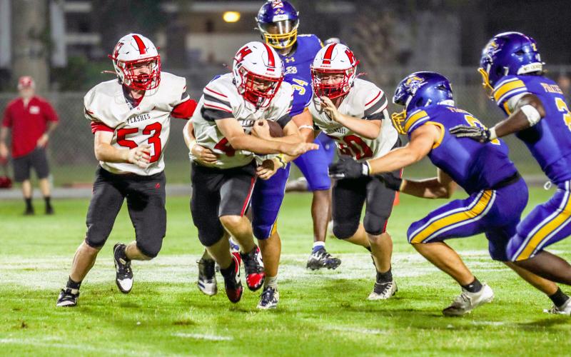 Tucker Williams tucks the ball in close as he runs past Pirates, flanked by teammates Brock McPherson and Anthony Musgrove.