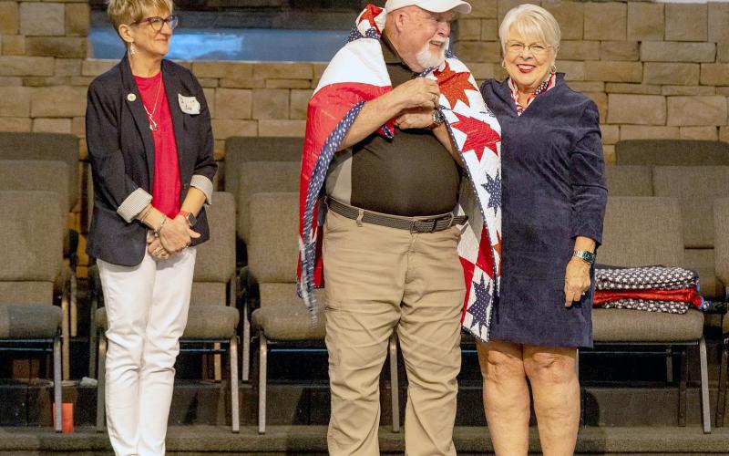 Country Star Quilt Guild members Lori Frederick and Sue Dayo wrap veteran Army Sgt. Eugene Merson in a Quilt of Valor. The guild members work together on a variety of sewing projects. A quilt will be raffled off later this fall as the group’s annual fundraiser. Submitted