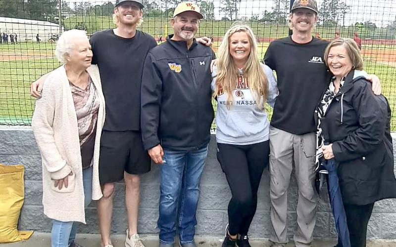West Nassau High School Principal Richard Pearce points at the sign bearing  his name at the building’s  dedication Monday evening.  He hugs current baseball Coach Micheal Henderson at left and is joined by family members above, including Jami Pearce, Ann Clarke, Lawana Nazworth, Cadin Whitehead, and Colin Whitehead. Pearce served as head coach of the Warriors for 17 years. Submitted