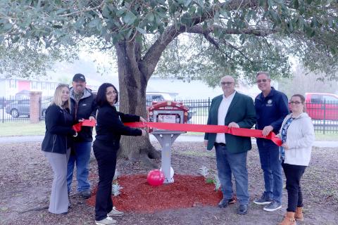 Dr. Kathia Ortiz cuts the ribbon joined by Nassau County commissioners Klynt Farmer and “Hupp” Huppmann, Callahan Town Clerk Shawna Gugliuzza, Callahan Mayor Randy Knagge, and Tiny Libraries of Nassau President Katey Kilpatrick. 