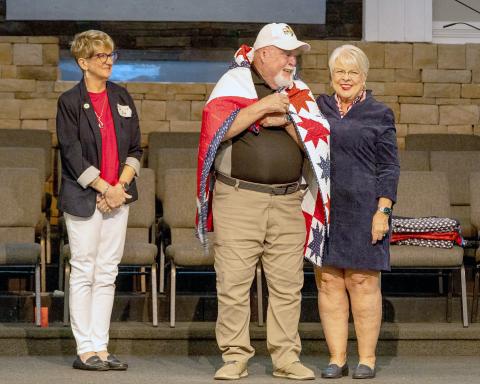 Country Star Quilt Guild members Lori Frederick and Sue Dayo wrap veteran Army Sgt. Eugene Merson in a Quilt of Valor. The guild members work together on a variety of sewing projects. A quilt will be raffled off later this fall as the group’s annual fundraiser. Submitted