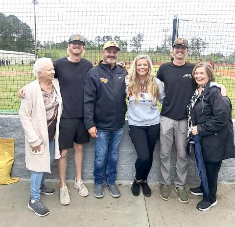 West Nassau High School Principal Richard Pearce points at the sign bearing  his name at the building’s  dedication Monday evening.  He hugs current baseball Coach Micheal Henderson at left and is joined by family members above, including Jami Pearce, Ann Clarke, Lawana Nazworth, Cadin Whitehead, and Colin Whitehead. Pearce served as head coach of the Warriors for 17 years. Submitted